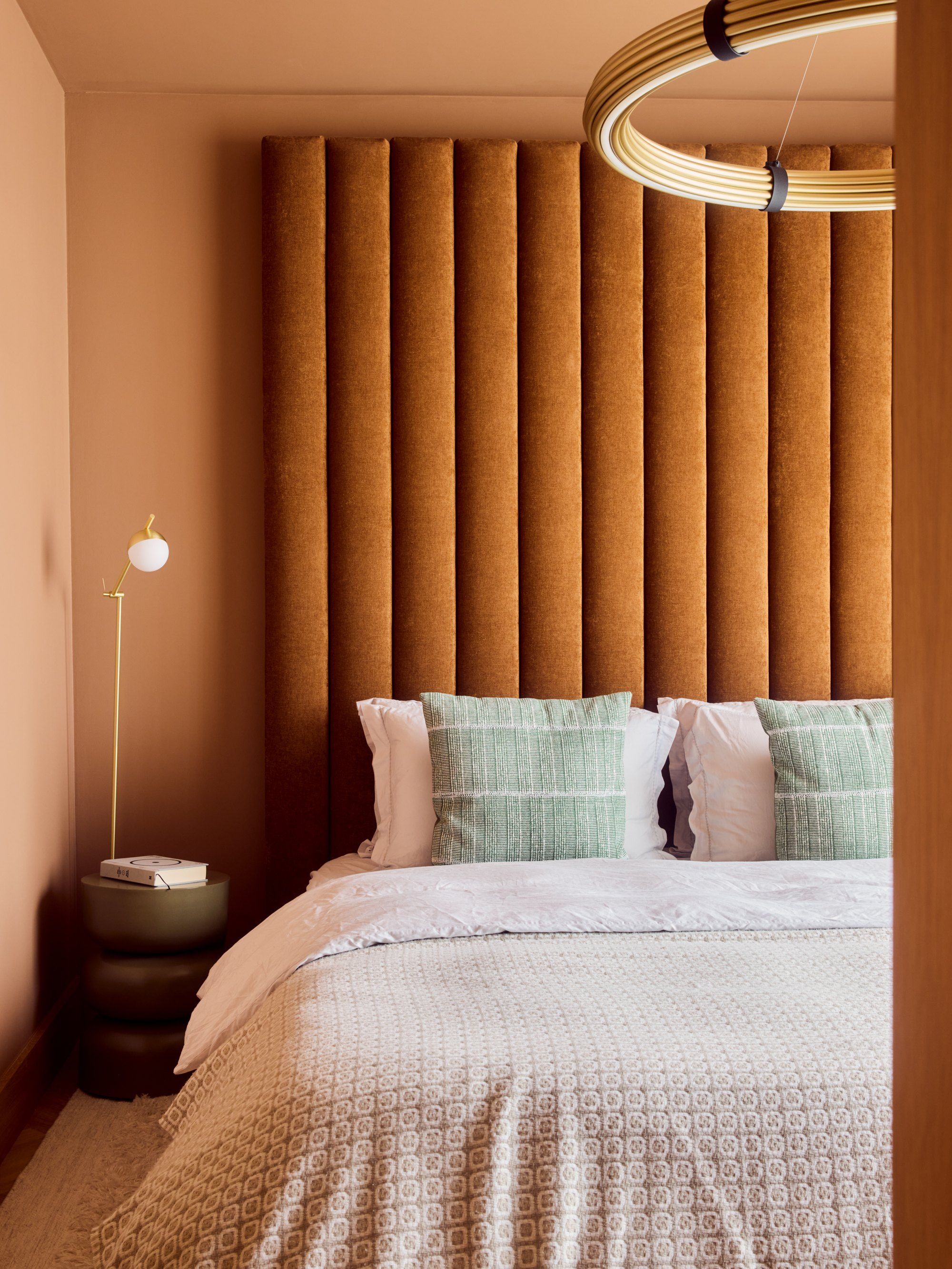 A bedroom with a full-height fluted headboard and a ring pendant