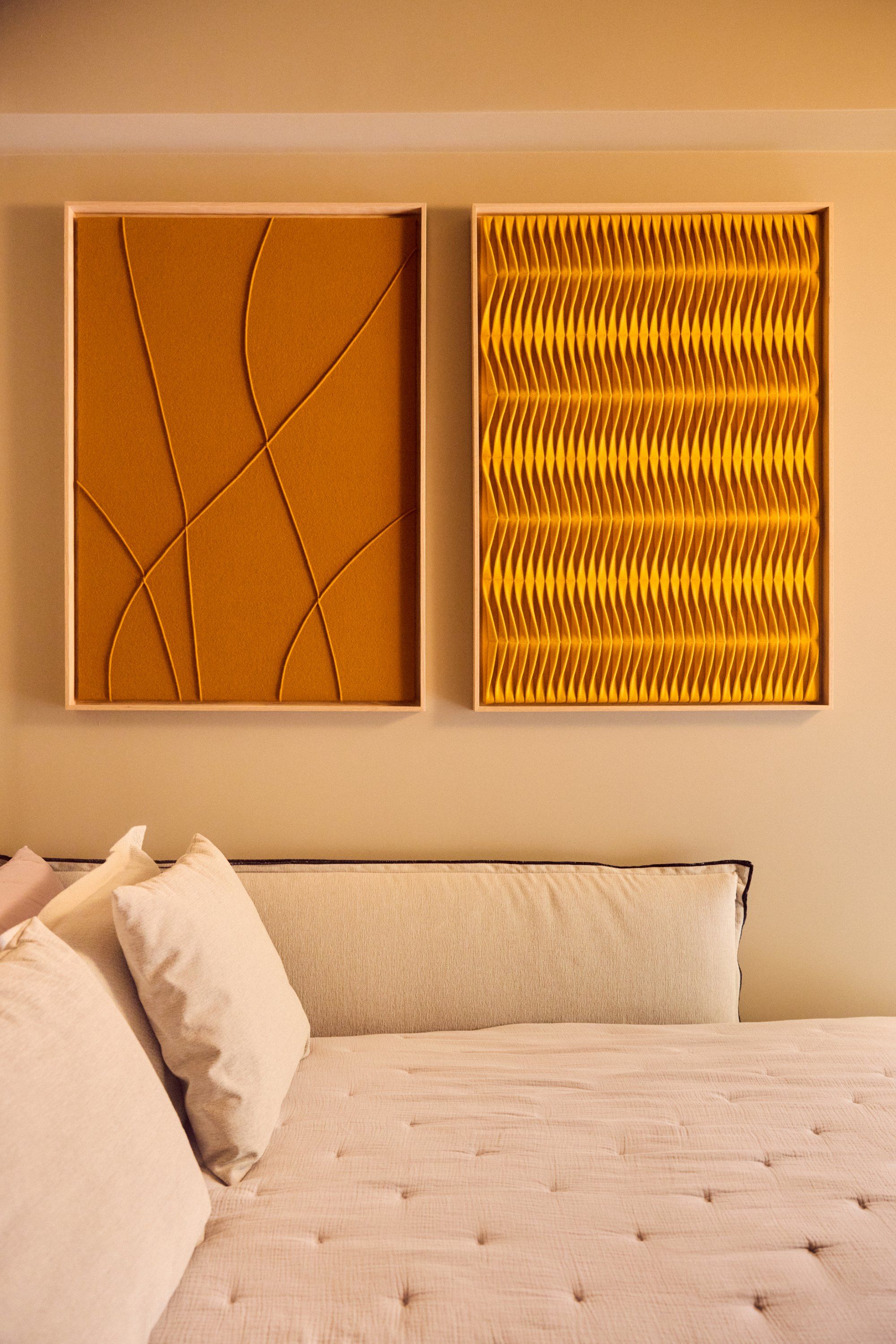 A second bedroom with two ochre artworks above a buttoned bed