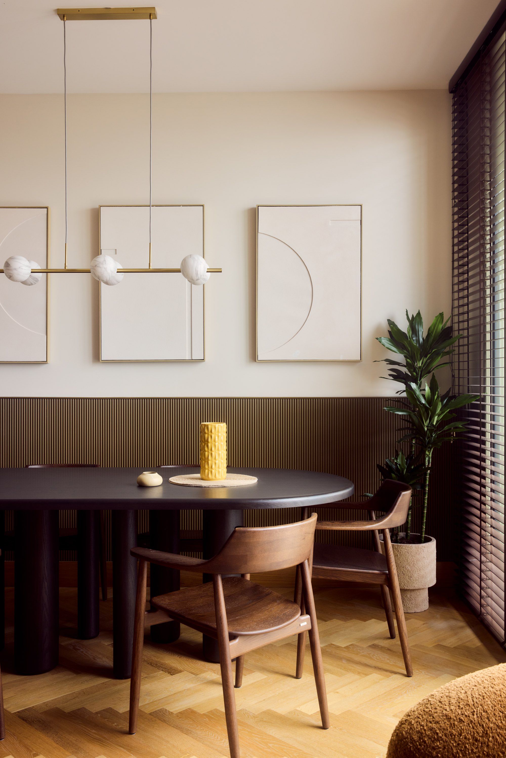 The dining room: an oval table, three framed works and a linear brass pendant
