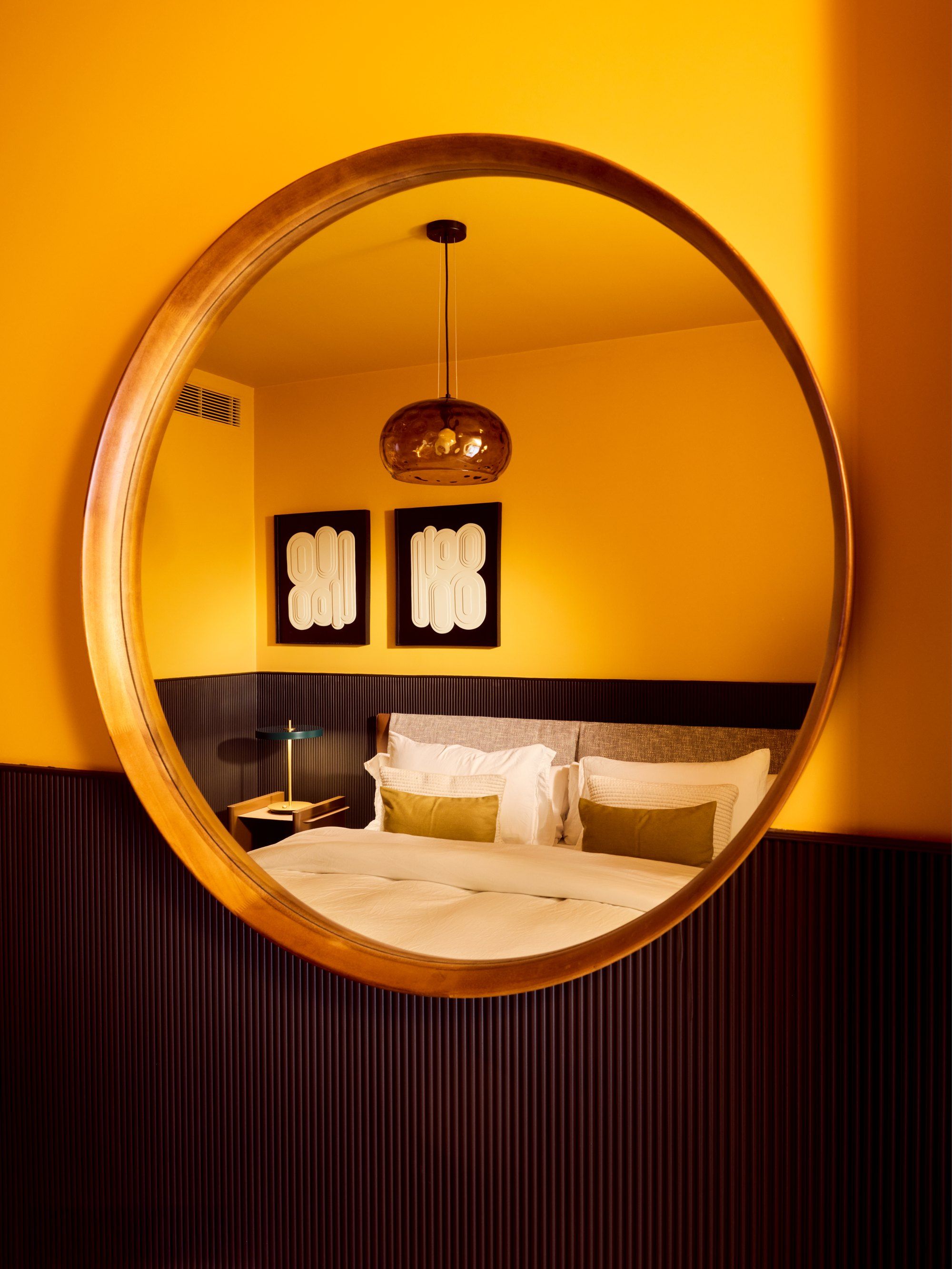 The same yellow bedroom seen in a large circular mirror
