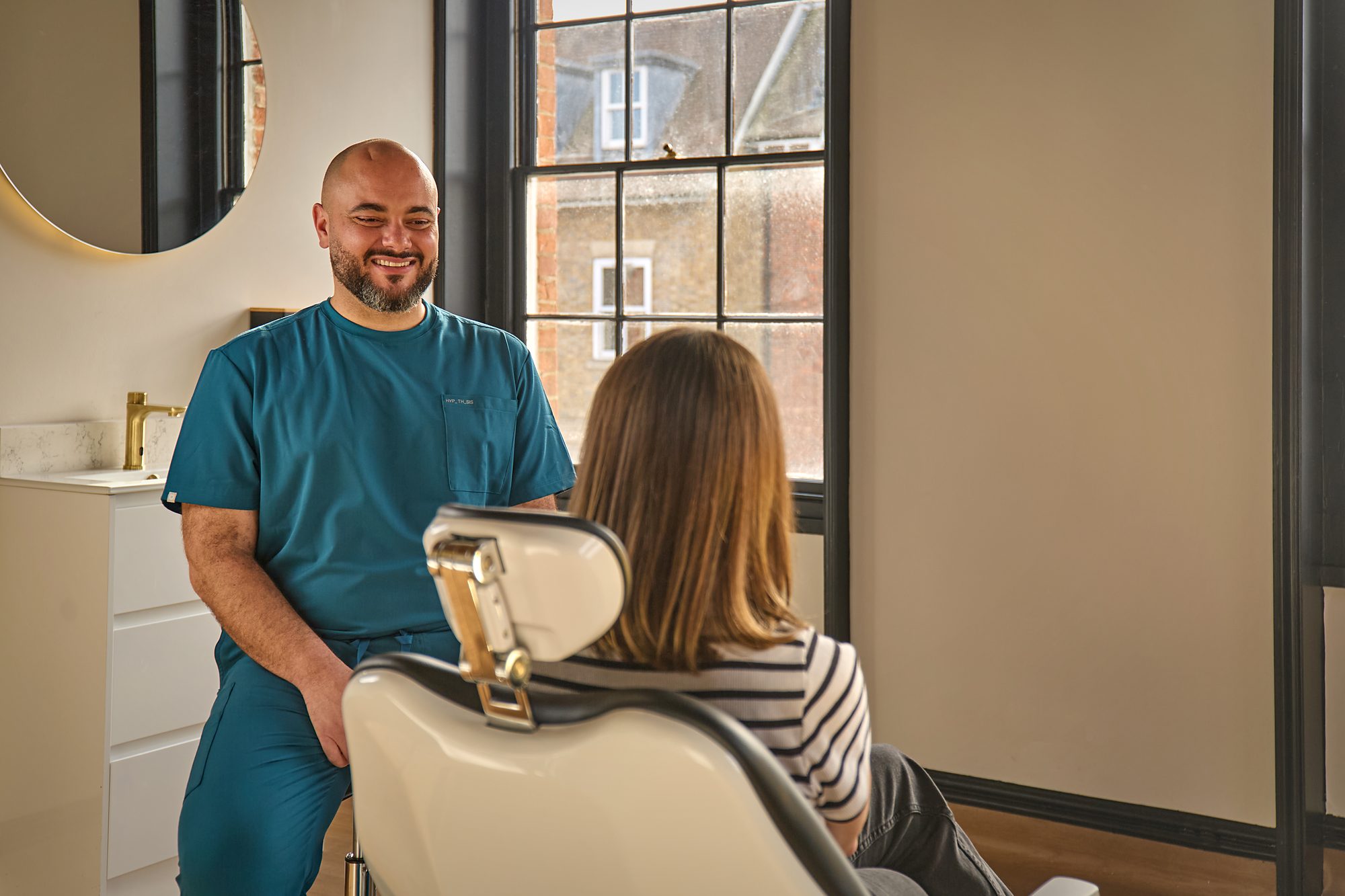 A clinician and a patient talking in a treatment room beside the windows
