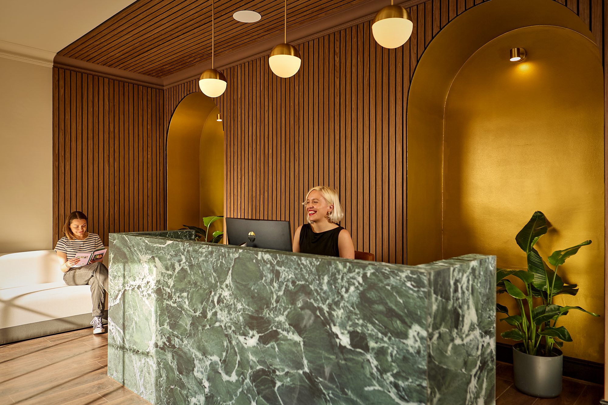 Reception staff at the green marble desk below the ochre arches