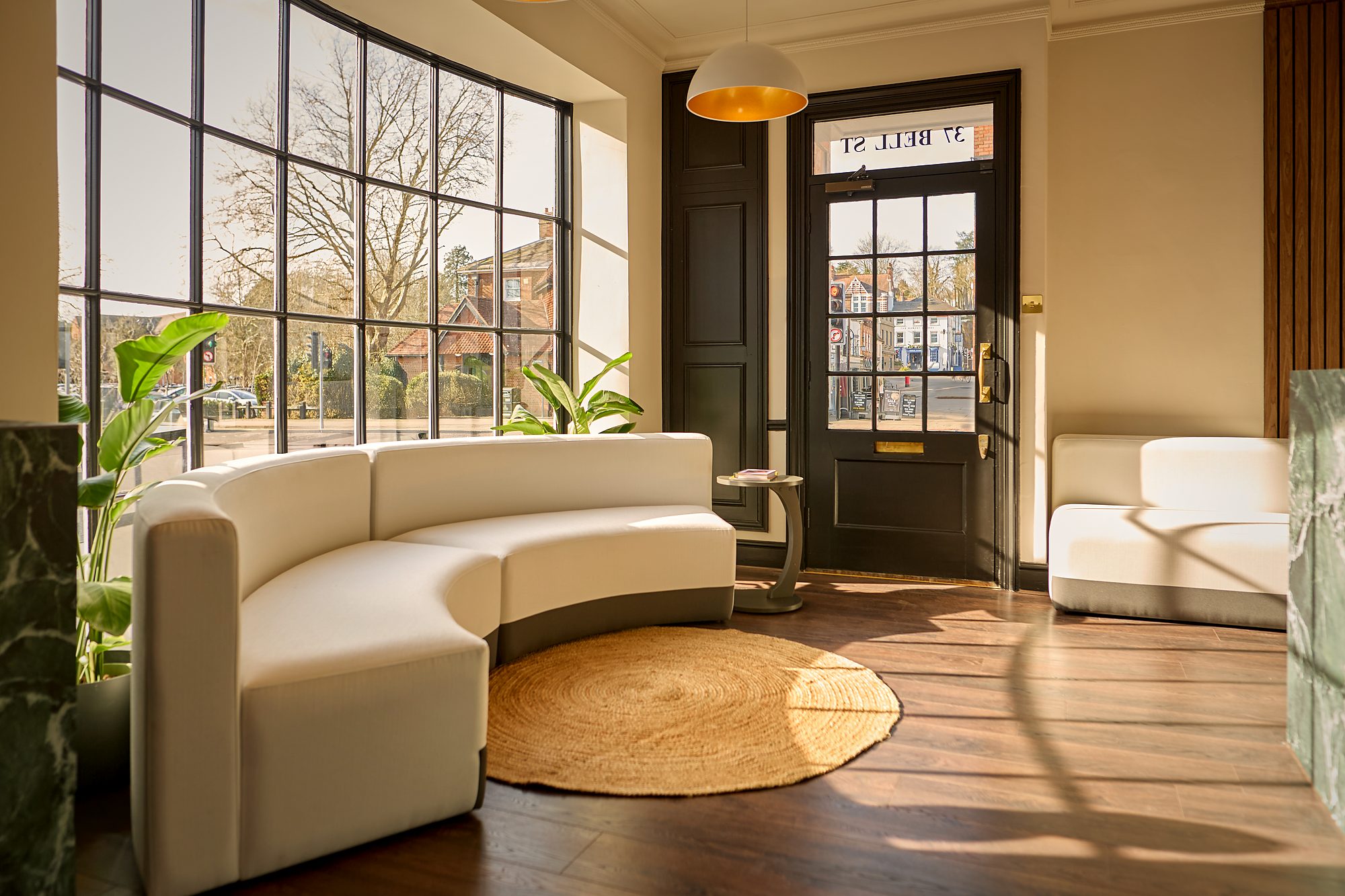 The waiting room as built: a curved cream sofa on a round jute rug over plank flooring, the front door and street beyond