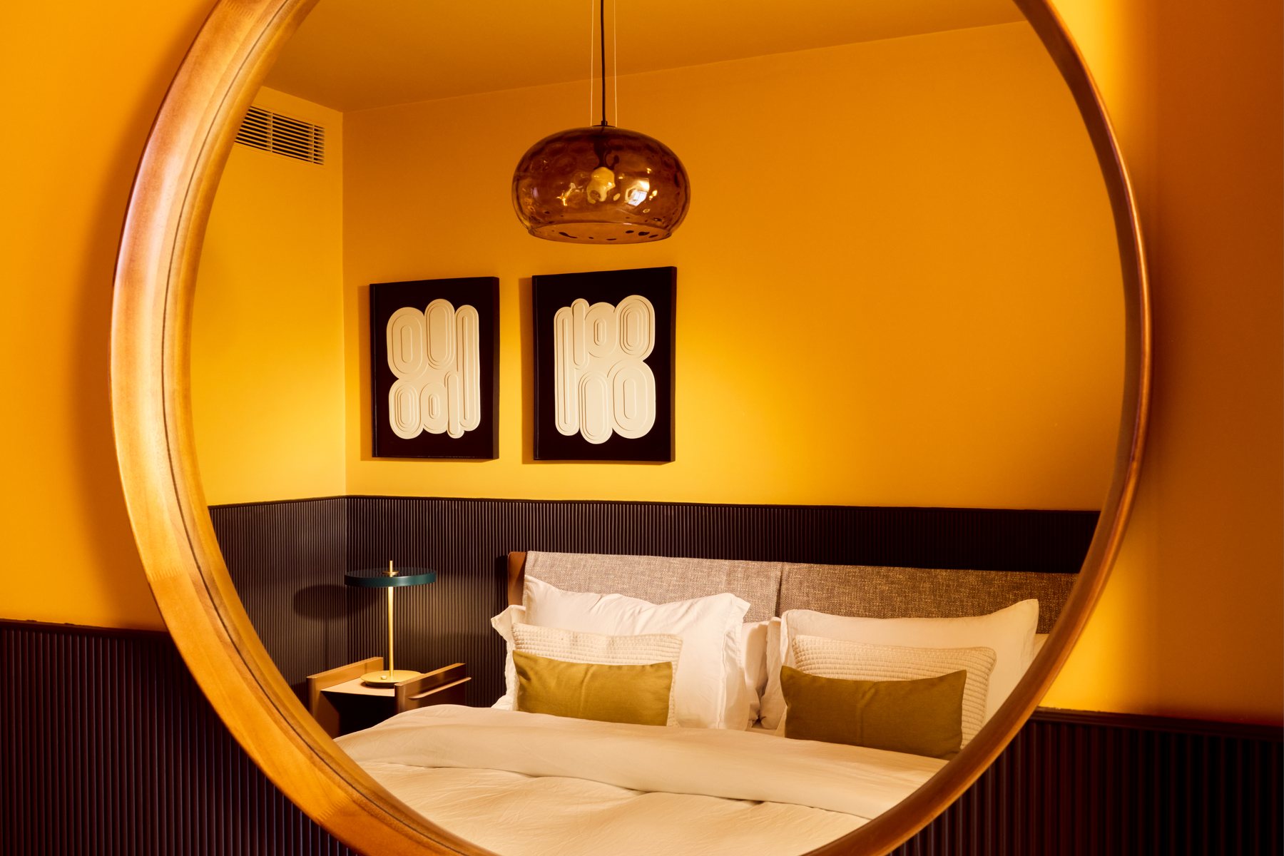 The finished room photographed in its round mirror: the two panels on the ochre wall, the dark fluted panelling, the green shaded lamp and the bed, all reflected
